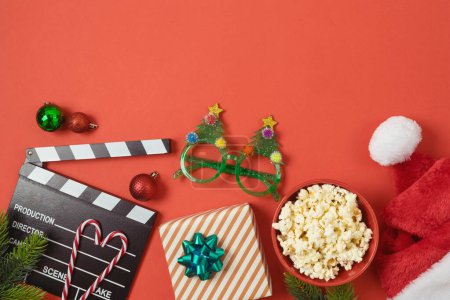 Photo for Christmas movie night and party concept with  popcorn, santa hat, decorations and movie clapper board on red background. Top view, flat lay - Royalty Free Image
