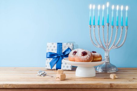 Foto de Concepto de Hanukkah fiesta judía con menorah, rosquillas tradicionales y caja de regalo en mesa de madera. - Imagen libre de derechos
