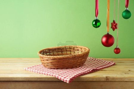 Foto de Cesta vacía sobre mesa de madera con decoración ornamentada colgante y mantel sobre fondo verde. Maqueta de Navidad para el diseño y la exhibición del producto. - Imagen libre de derechos