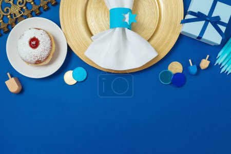 Foto de Composición plana para Hanukkah vacaciones con plato de oro, rosquillas tradicionales, menorah y caja de regalo sobre fondo azul. Vista superior. - Imagen libre de derechos
