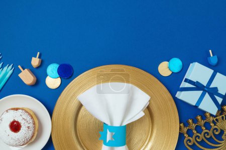 Photo for Jewish holiday Hanukkah border background with golden plate, traditional donuts, menorah and gift box on blue tabletop. Top view, flat lay - Royalty Free Image