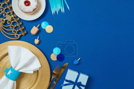 Photo for Hanukkah table setting concept with plate, stylish cutlery, gift box and traditional donuts on blue background. Top view, flat lay - Royalty Free Image