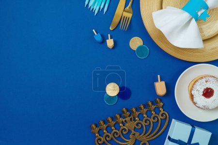 Téléchargez les photos : Concept de table Hanukkah avec assiette, couverts élégants, coffret cadeau et beignets traditionnels sur fond bleu. Vue de dessus, plan plat - en image libre de droit