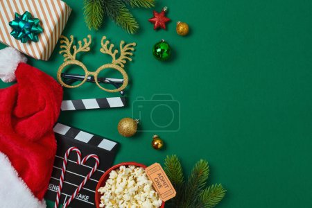 Foto de Noche de cine de Navidad y concepto de fiesta con palomitas de maíz, sombrero de Santa, decoraciones y tablero de aplausos de película sobre fondo verde. Vista superior, plano - Imagen libre de derechos