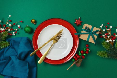 Téléchargez les photos : Joyeux Noël et Bonne Année concept avec assiette, boîte cadeau et décorations sur fond vert. Vue de dessus, plan plat - en image libre de droit