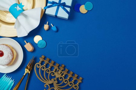 Téléchargez les photos : Noël juif Hanoukka concept avec plaque d'or, beignets traditionnels, menorah et boîte cadeau sur fond bleu. Vue de dessus, plan plat - en image libre de droit