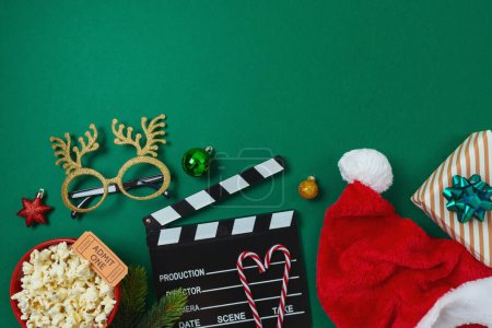 Foto de Noche de cine de Navidad y concepto de fiesta con palomitas de maíz, sombrero de Santa, decoraciones y tablero de aplausos de película sobre fondo verde. Vista superior, plano - Imagen libre de derechos