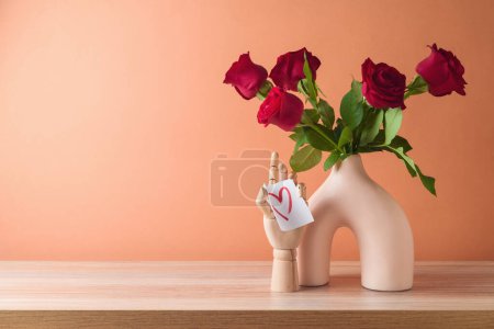 Foto de San Valentín romántico bodegón con ramo de rosas rojas en florero moderno sobre mesa de madera sobre fondo de color melocotón - Imagen libre de derechos