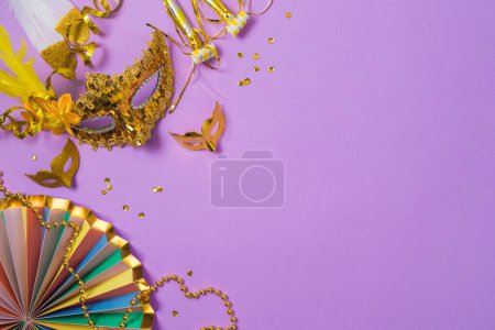 Foto de Concepto de carnaval o mardi gras con máscaras de carnaval dorado y decoraciones de fiesta sobre fondo púrpura. Vista superior, plano - Imagen libre de derechos