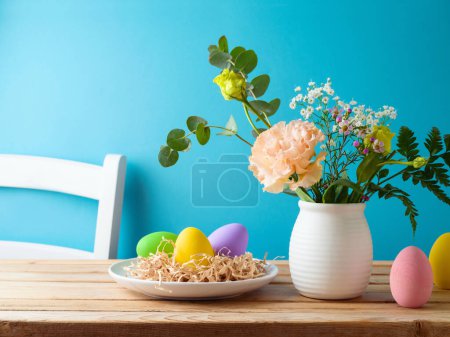 Foto de Decoración de huevos de Pascua y ramo de flores en mesa de madera sobre fondo azul - Imagen libre de derechos
