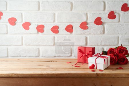Téléchargez les photos : Fond Saint-Valentin avec table en bois vide, boîte cadeau et forme de coeur sur un mur de briques. Modèle de vacances pour le design et l'affichage des produits - en image libre de droit