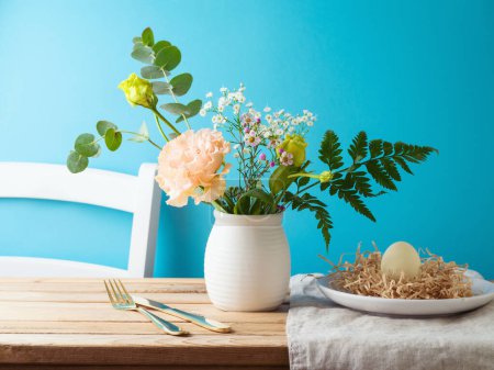 Foto de Ramo de flores y plato de Pascua con decoración de huevos de Pascua en mesa de madera sobre fondo azul - Imagen libre de derechos