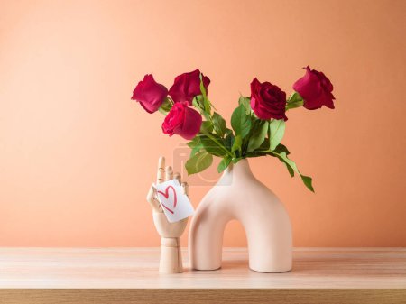 Foto de San Valentín romántico bodegón con ramo de rosas rojas en florero moderno sobre mesa de madera sobre fondo de color melocotón - Imagen libre de derechos