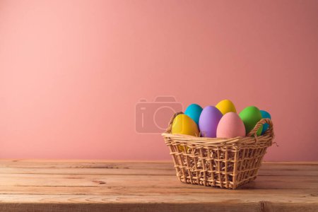 Foto de Concepto de vacaciones de Pascua con huevos de Pascua en cesta sobre mesa de madera sobre fondo rosa - Imagen libre de derechos