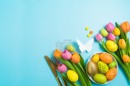 Foto de Concepto de celebración de Pascua con huevos de Pascua cubiertos de oro y flores de tulipán sobre fondo azul. Vista superior, composición plana - Imagen libre de derechos