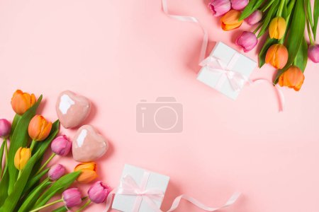 Téléchargez les photos : Joyeux concept de fête des mères avec des fleurs de tulipes, forme de coeur et boîte cadeau sur fond rose. Vue de dessus. Composition de la couche plane - en image libre de droit