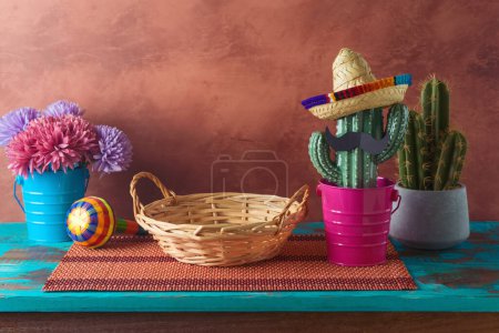 Foto de Cesta de mimbre vacía sobre mesa azul madera con decoración de cactus sobre fondo de pared. Maqueta de fiesta mexicana para diseño y exhibición de productos - Imagen libre de derechos