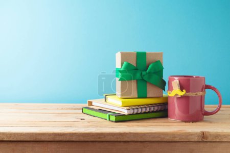 Foto de Concepto del día del padre feliz con taza de café colorida, bigote, cuaderno y caja de regalo en la mesa de madera sobre fondo azul - Imagen libre de derechos