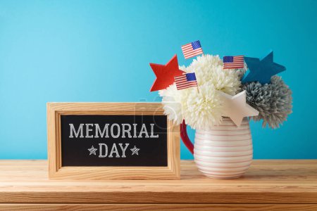 Foto de Concepto de día conmemorativo con decoración de flores, pizarra y banderas de EE.UU. sobre mesa de madera sobre fondo azul - Imagen libre de derechos