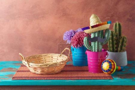 Leerer Weidenkorb auf blauem Holztisch mit Kakteendekoration über dem Wandhintergrund. Mexikanische Party-Attrappe für Design und Produktpräsentation