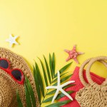 Summer vacation concept with straw hat, bag, palm tree leaf and beach accessories on yellow background. Top view, flat lay
