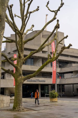 Foto de LONDRES - 21 de abril de 2023: Disfrute de las vistas del Teatro Nacional de Southbank en un día gris, con un árbol desnudo recientemente recortado que agrega a la belleza natural del paisaje urbano. - Imagen libre de derechos