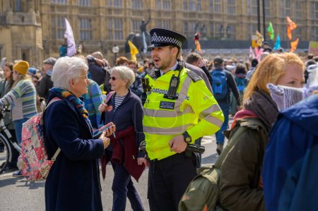 Téléchargez les photos : LONDRES - 22 avril 2023 : Lien humain au milieu de l'activisme : Un policier métropolitain engage un dialogue avec une femme âgée lors d'une manifestation de rébellion contre l'extinction devant les chambres du Parlement de Londres. - en image libre de droit