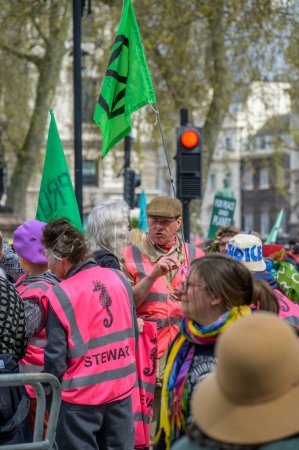Foto de LONDRES - 22 de abril de 2023: Seguridad de la marcha XR: Mayordomos en acción en la protesta de Londres, con chaquetas de alta visibilidad para el control de multitudes y la gestión de la seguridad. - Imagen libre de derechos