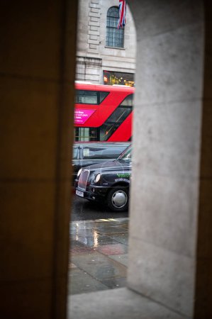 Foto de LONDRES - 24 de abril de 2023: Una escena clásica de Londres: Un autobús rojo de dos pisos y un taxi negro enmarcado por un arco en un día lluvioso, personificando la vida urbana británica. - Imagen libre de derechos