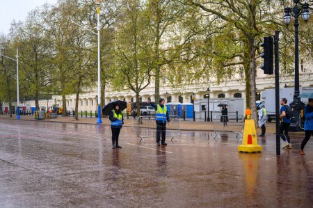 Foto de LONDRES - 24 de abril de 2023: Los mayordomos con chaquetas reflectantes trabajan en un día lluvioso, dirigiendo a los peatones en el centro comercial antes de la coronación del rey Carlos. - Imagen libre de derechos