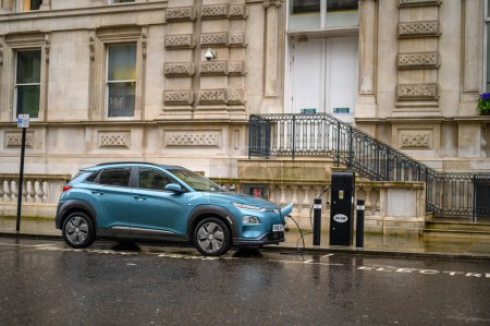 Foto de LONDRES - 24 de abril de 2023: Un coche eléctrico se carga en una calle húmeda de Londres, mostrando una vida urbana sostenible en un día lluvioso. - Imagen libre de derechos