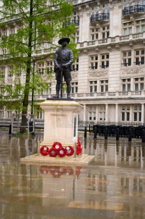 Foto de LONDRES - 24 de abril de 2023: La estatua del soldado Gurkha se encuentra entre las coronas de amapola rojas fuera del Ministerio de Defensa, con un suelo húmedo reflectante que se suma al tributo. - Imagen libre de derechos
