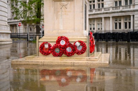 Foto de LONDRES - 24 de abril de 2023: Las coronas rojas de amapola en la base de la estatua del soldado Gurkha con reflexiones sobre el pavimento húmedo crean una escena conmovedora fuera del Ministerio de Defensa. - Imagen libre de derechos