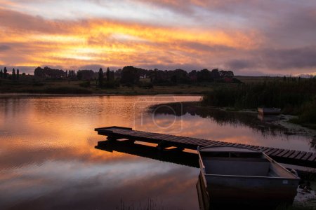 Photo for Striking sunrise over a body of water with a jetty and a small moored boat - Royalty Free Image