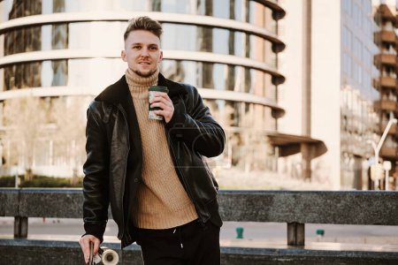 Téléchargez les photos : Portrait d'un jeune homme caucsien avec un skateboard buvant du café à emporter dans la rue - en image libre de droit