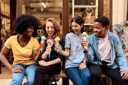 Téléchargez les photos : Vue frontale d'un groupe multiethnique d'amis célébrant en mangeant de la crème glacée à l'extérieur - en image libre de droit