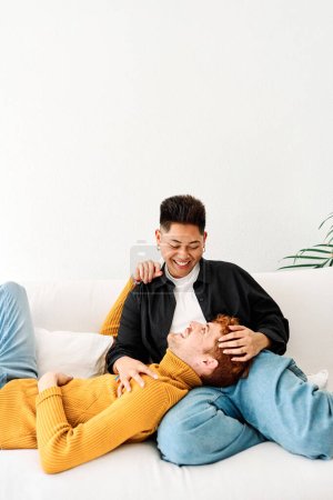 Téléchargez les photos : Photo verticale d'un homme allongé sur les genoux de son couple gay dans le canapé à la maison - en image libre de droit