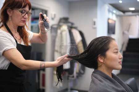 Hairstylist dampening the hair of a chinese woman to wet it in the salon