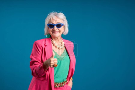 Encantadora mujer mayor abandonando pulgares en chaqueta rosa