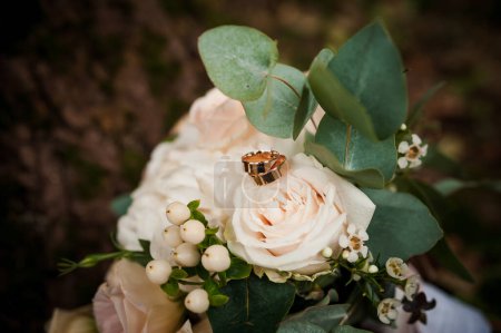 A pair of gold wedding rings on a bouquet of white flowers. Gold rings on a bouquet of roses