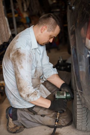 Ein Mechaniker repariert ein Auto-Fahrgestell. Ein Mann entfernt Autoräder mit einem Schraubenzieher