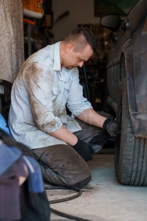 Ein Mechaniker repariert ein Auto-Fahrgestell. Ein Mann entfernt Autoräder mit einem Schraubenzieher
