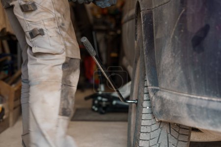 Foto de Un mecánico repara un chasis de coche. Un hombre quita las ruedas del coche con un destornillador - Imagen libre de derechos