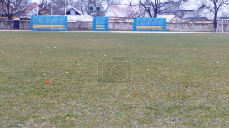 A view of an empty football field covered in grass with gates and stands for spectators, in winter during cold season