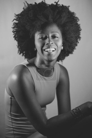 Téléchargez les photos : Heureuse femme afro-américaine aux cheveux bouclés souriant et regardant la caméra sous la lumière violette au néon. Photographie noir et blanc. - en image libre de droit