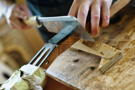 Photo for Crop male artisan using sharp knife to cut wood, marking the frets on neck of Spanish flamenco guitar during work in professional luthier workshop - Royalty Free Image
