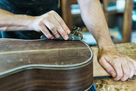 Photo for Crop craftsman using plane to shave traditional Spanish flamenco guitar on workbench in workshop - Royalty Free Image