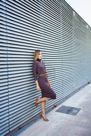 Foto de Full body female entrepreneur in stylish dress and high heeled shoes leaning on metal wall of modern building on city street - Imagen libre de derechos