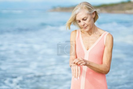 Photo for Beautiful mature woman walking along the shore of a tropical beach, wearing a nice orange dress. Elderly female enjoying her retirement at a seaside retreat. - Royalty Free Image