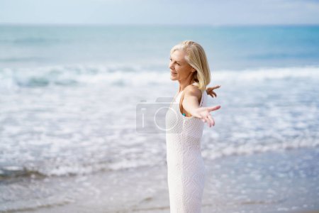 Téléchargez les photos : Femme mûre ouvrant les bras sur une plage tropicale, passant son temps libre. Femme âgée profitant de sa retraite dans une retraite au bord de la mer. - en image libre de droit
